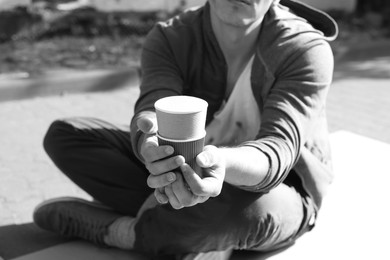 Photo of Homeless man with paper cups begging for money outdoors, closeup. Black and white effect
