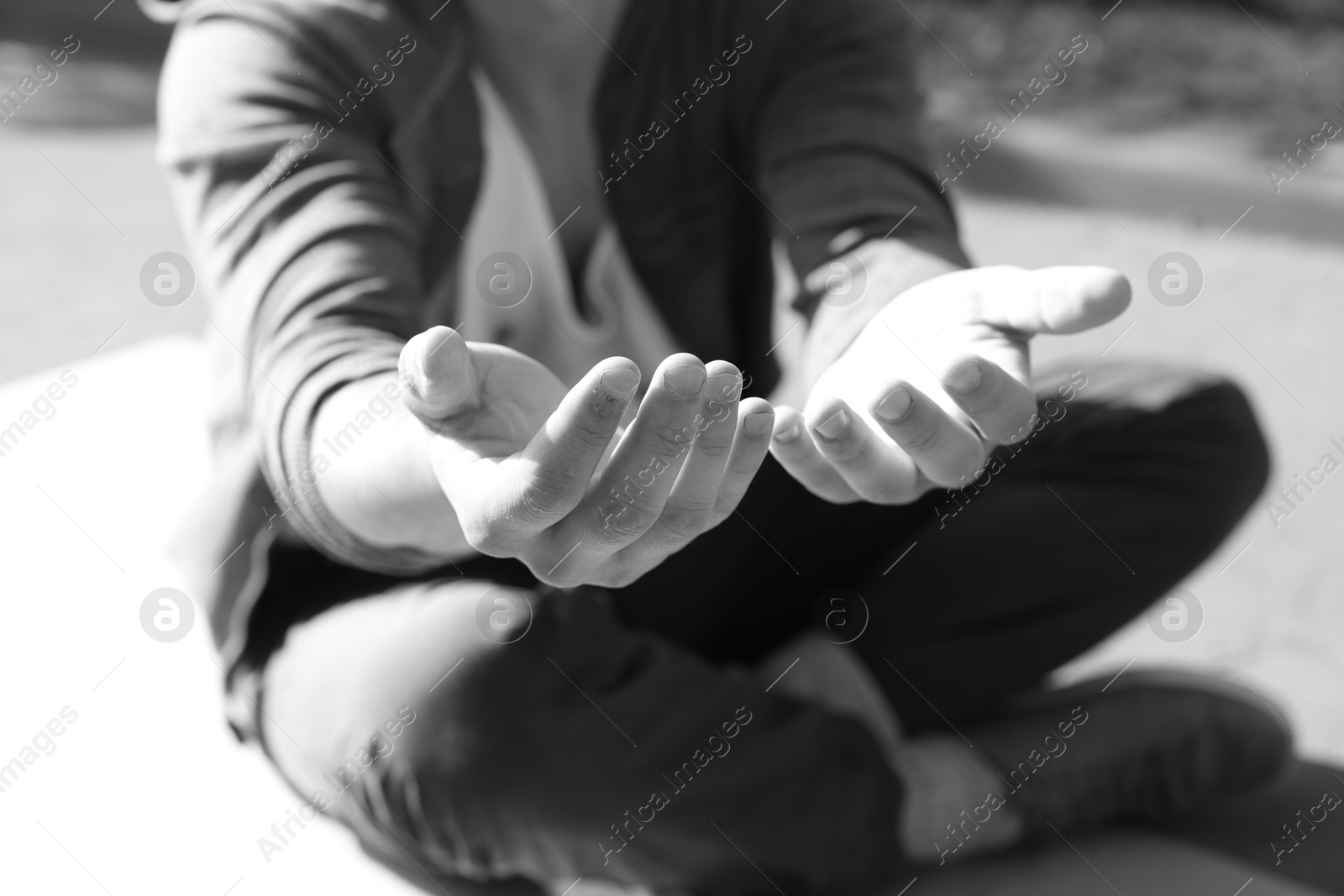 Photo of Homeless man begging for money on carton outdoors, closeup. Black and white effect