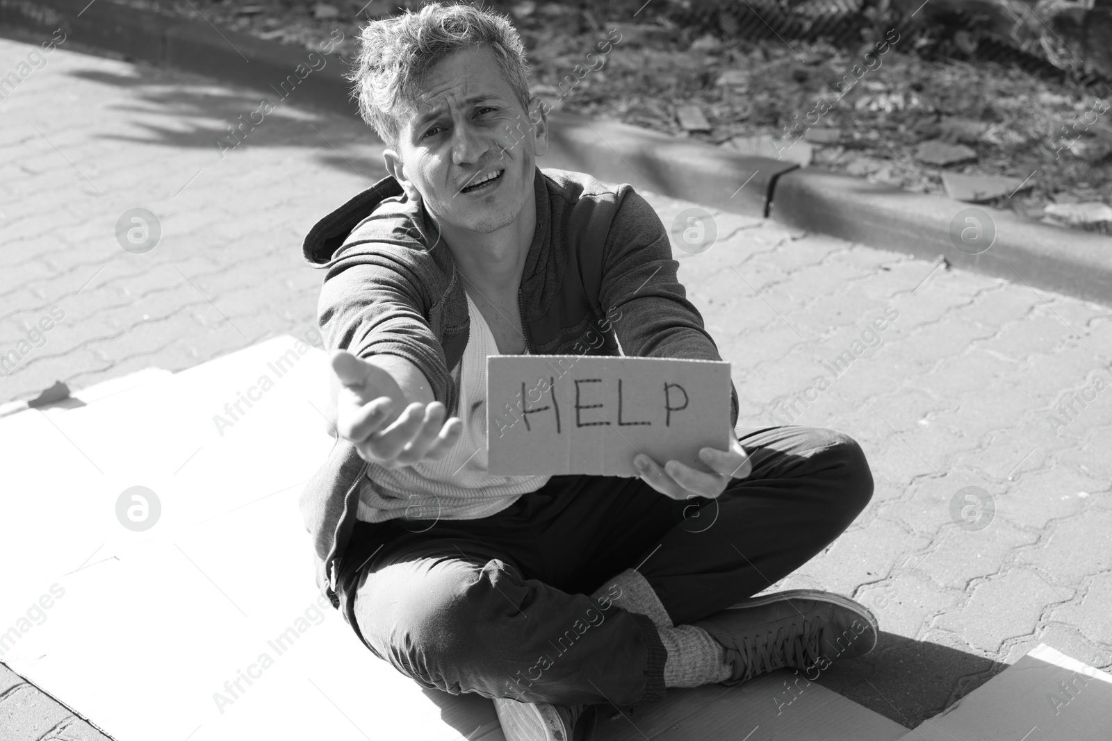 Photo of Homeless man with sign Help begging for money on carton outdoors. Black and white effect