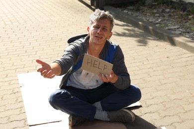 Photo of Homeless man with sign Help begging for money on carton outdoors