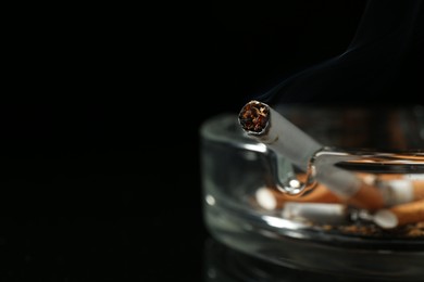 Photo of Cigarette butts in ashtray on black background, closeup. Space for text