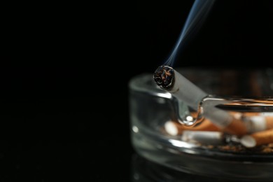 Photo of Cigarette butts in ashtray on black background, closeup. Space for text