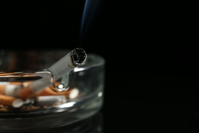 Photo of Cigarette butts in ashtray on black background, closeup. Space for text