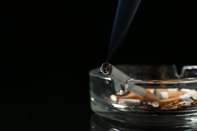 Photo of Cigarette butts in ashtray on black background, closeup. Space for text