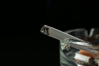 Photo of Cigarette butts in ashtray on black background, closeup. Space for text