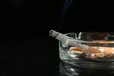 Photo of Cigarette butts in ashtray on black background, closeup. Space for text