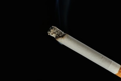 Photo of One burning cigarette on black background, closeup. Space for text