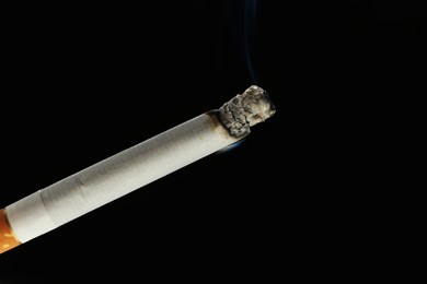 Photo of One burning cigarette on black background, closeup