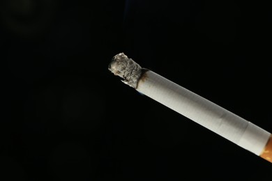 Photo of One burning cigarette on black background, closeup. Space for text