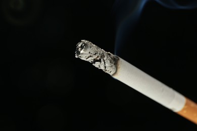 Photo of One burning cigarette on black background, closeup. Space for text