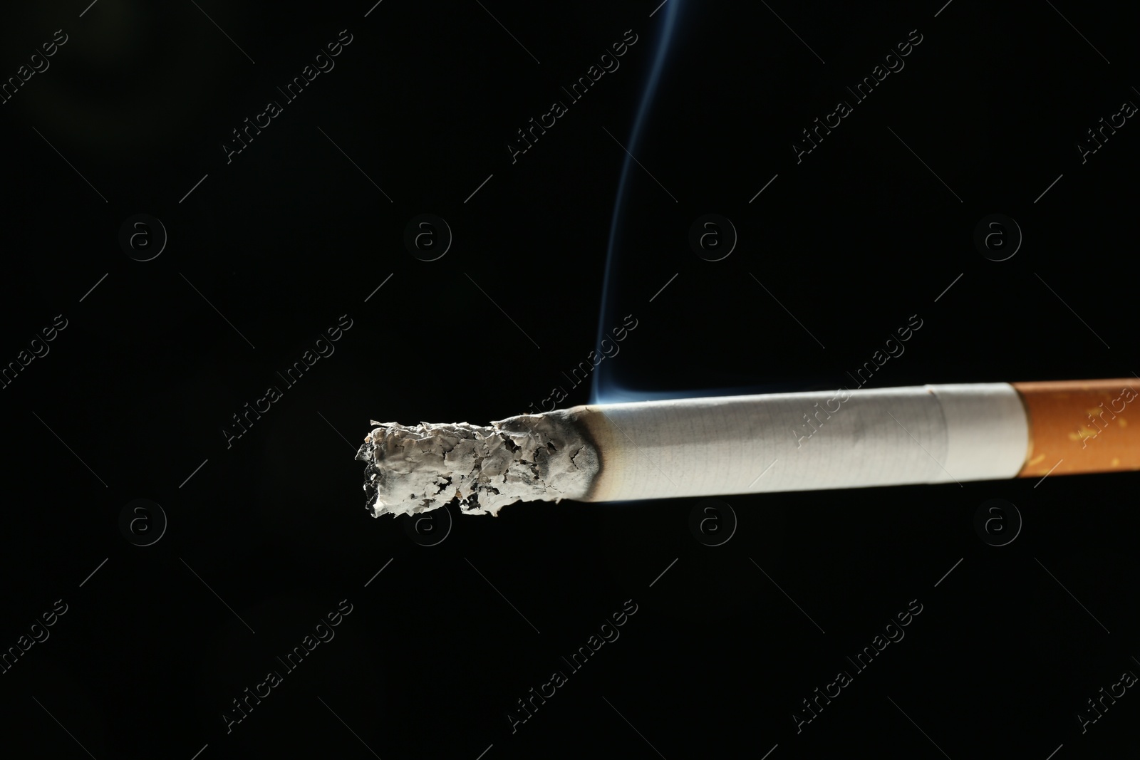 Photo of One burning cigarette on black background, closeup