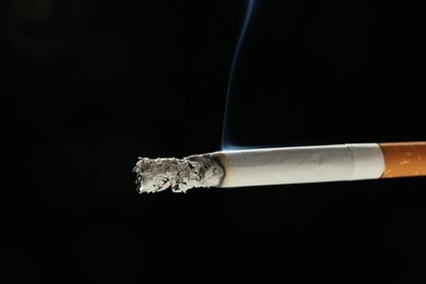 Photo of One burning cigarette on black background, closeup