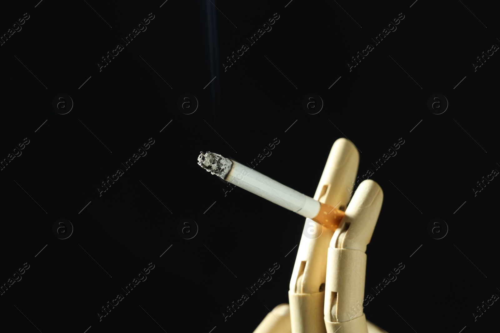 Wooden hand figure with burning cigarette on black background, closeup. Space for text Photo of Wooden hand figure with burning cigarette on black background, closeup. Space for text