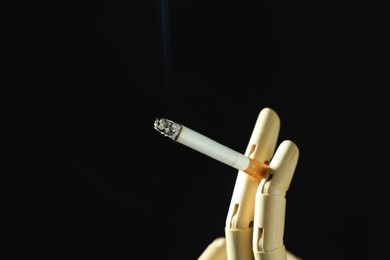 Photo of Wooden hand figure with burning cigarette on black background, closeup. Space for text