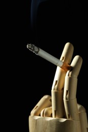 Photo of Wooden hand figure with burning cigarette on black background, closeup