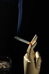 Photo of Wooden hand figure with burning cigarette on black background, closeup