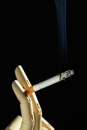 Photo of Wooden hand figure with burning cigarette on black background, closeup