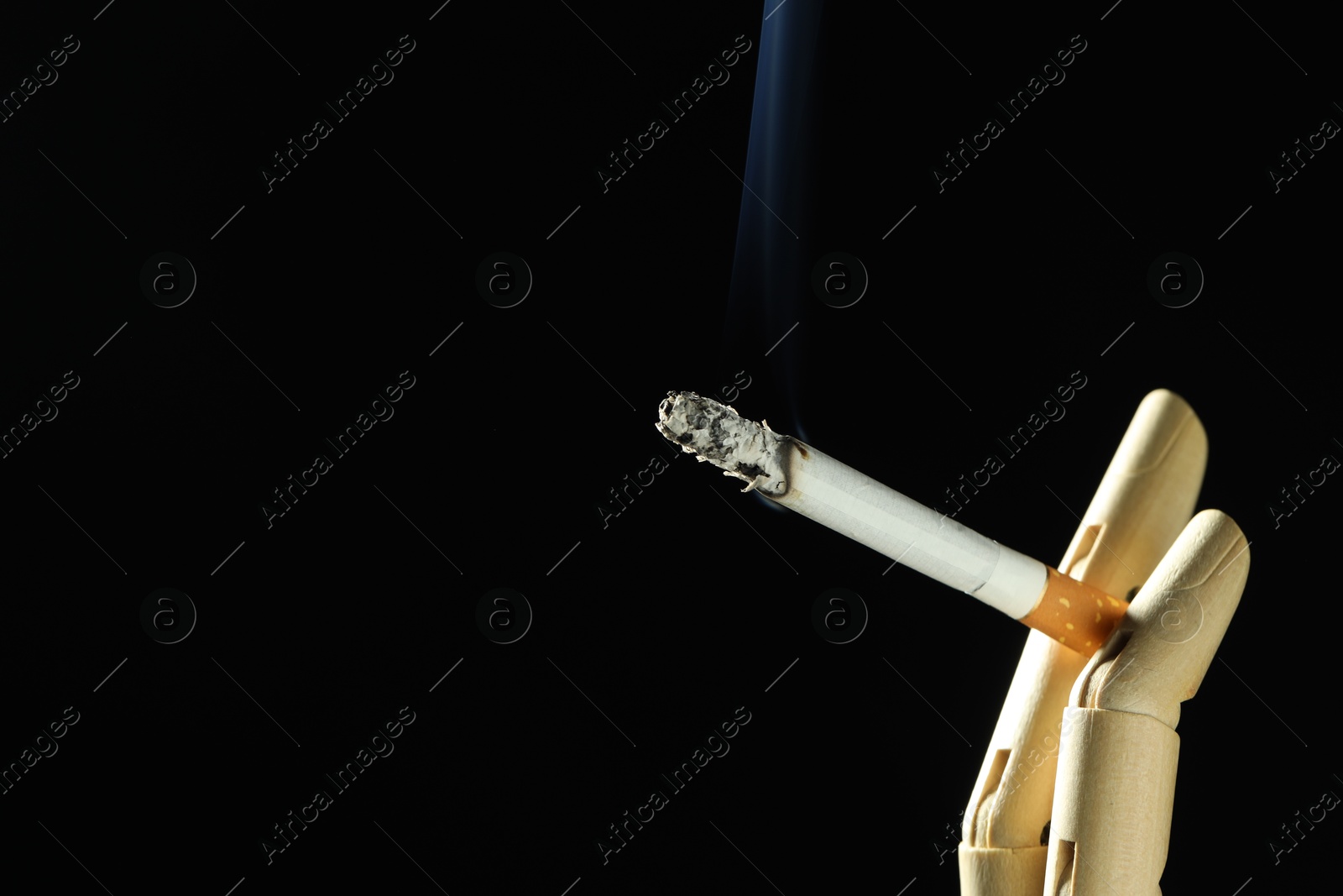 Wooden hand figure with burning cigarette on black background, closeup. Space for text Photo of Wooden hand figure with burning cigarette on black background, closeup. Space for text