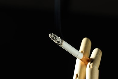Photo of Wooden hand figure with burning cigarette on black background, closeup. Space for text