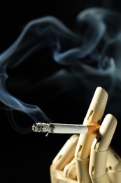 Photo of Wooden hand figure with burning cigarette on black background, closeup