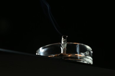 Photo of Cigarette butts in ashtray on black background, closeup