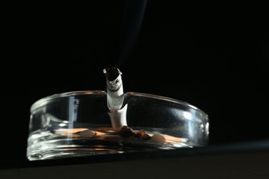 Photo of Cigarette butts in ashtray on black background, closeup