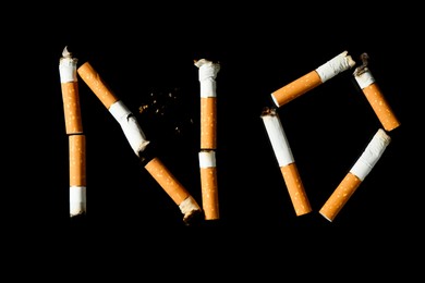 Photo of Word NO made with cigarette butts on black background, top view