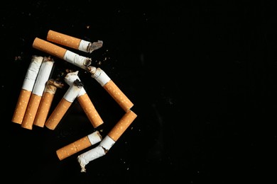 Photo of Cigarette butts with ash on black background, flat lay. Space for text