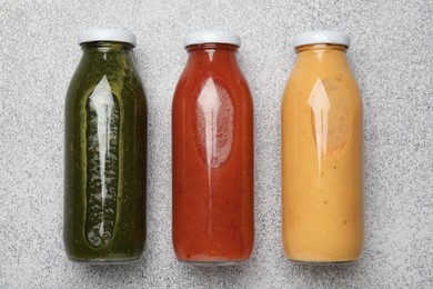 Photo of Superfood. Tasty smoothies in glass bottles on light grey table, flat lay