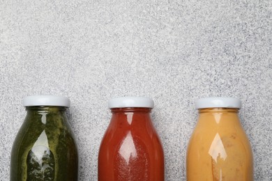 Photo of Superfood. Tasty smoothies in glass bottles on light grey table, flat lay. Space for text