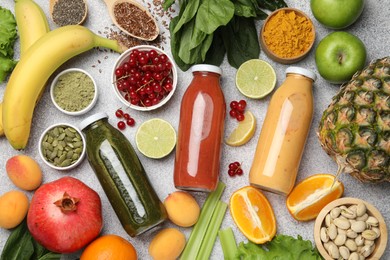 Photo of Superfood. Tasty smoothies in glass bottles and ingredients on light grey table, flat lay