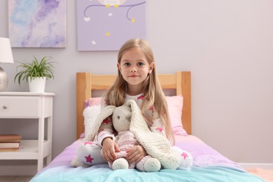 Photo of Cute little girl with toy bunny on bed at home