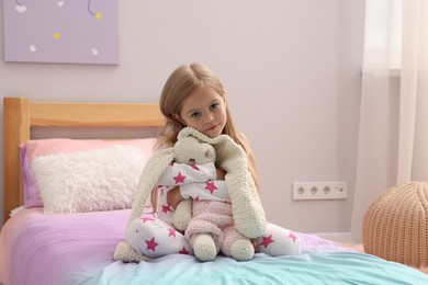 Photo of Cute little girl with toy bunny on bed at home