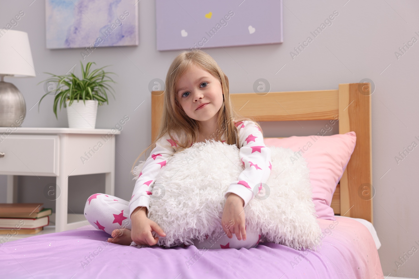 Cute little girl with pillow on bed at home Photo of Cute little girl with pillow on bed at home