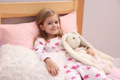 Photo of Cute little girl with toy bunny on bed at home