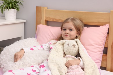 Photo of Cute little girl with toy bunny on bed at home