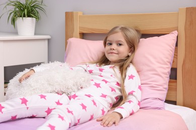 Photo of Cute little girl with pillow on bed at home