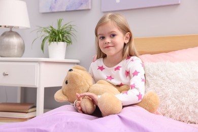 Photo of Cute little girl with teddy bear on bed at home