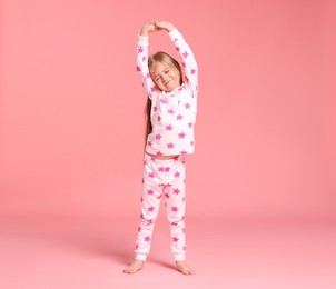 Photo of Cute little girl in pajamas stretching on pink background