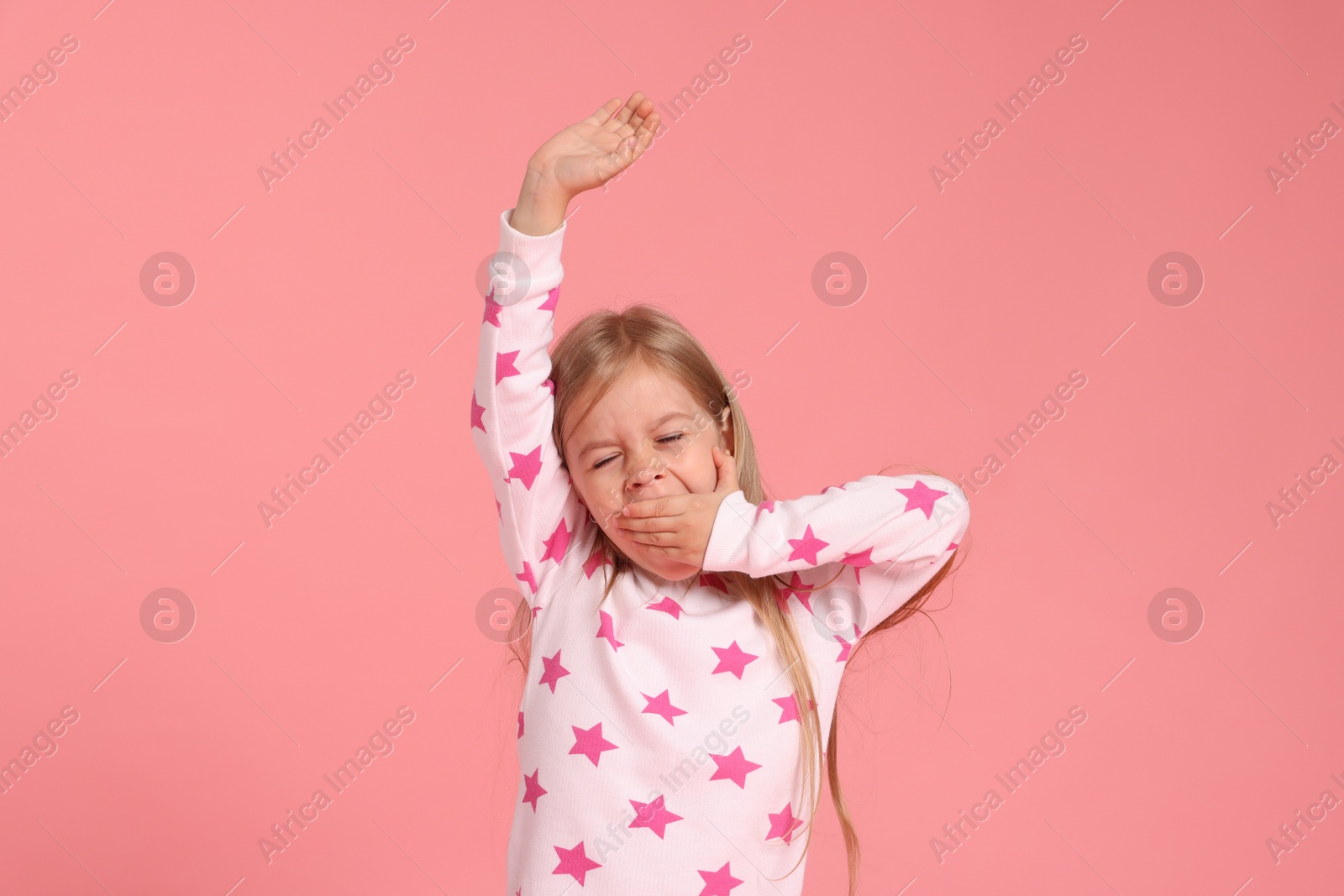 Cute little girl in pajamas yawning on pink background Photo of Cute little girl in pajamas yawning on pink background