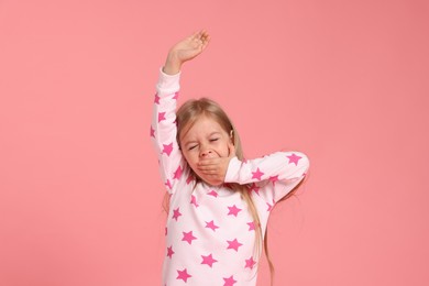 Photo of Cute little girl in pajamas yawning on pink background