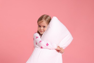 Photo of Cute little girl in pajamas with pillow on pink background