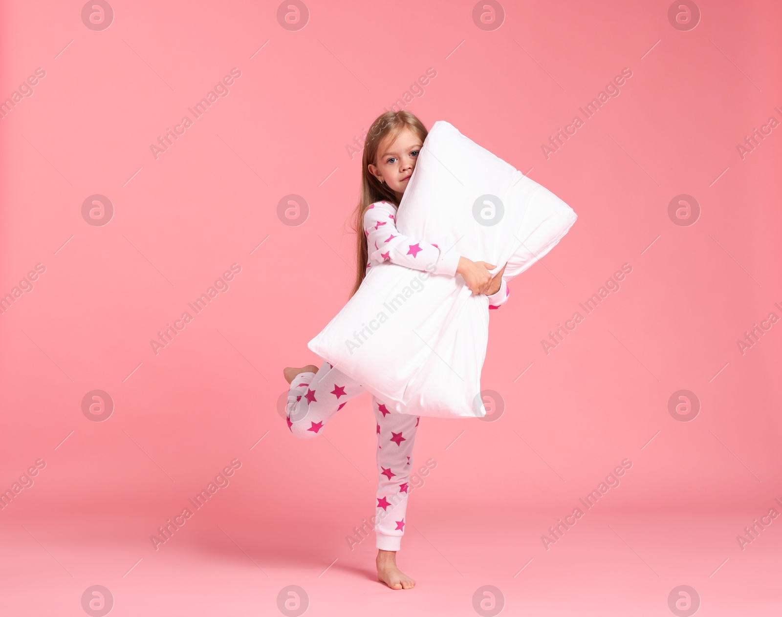 Cute little girl in pajamas with pillow on pink background Photo of Cute little girl in pajamas with pillow on pink background
