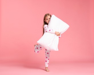 Photo of Cute little girl in pajamas with pillow on pink background
