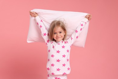 Photo of Cute little girl in pajamas with pillow on pink background