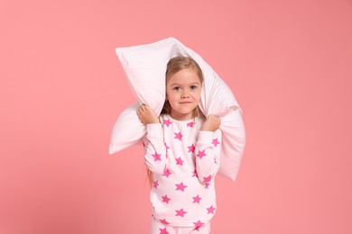 Photo of Cute little girl in pajamas with pillow on pink background