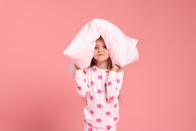 Photo of Cute little girl in pajamas with pillow on pink background