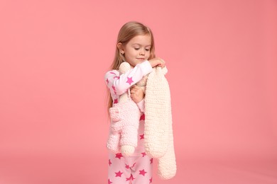 Photo of Cute little girl in pajamas with toy bunny on pink background