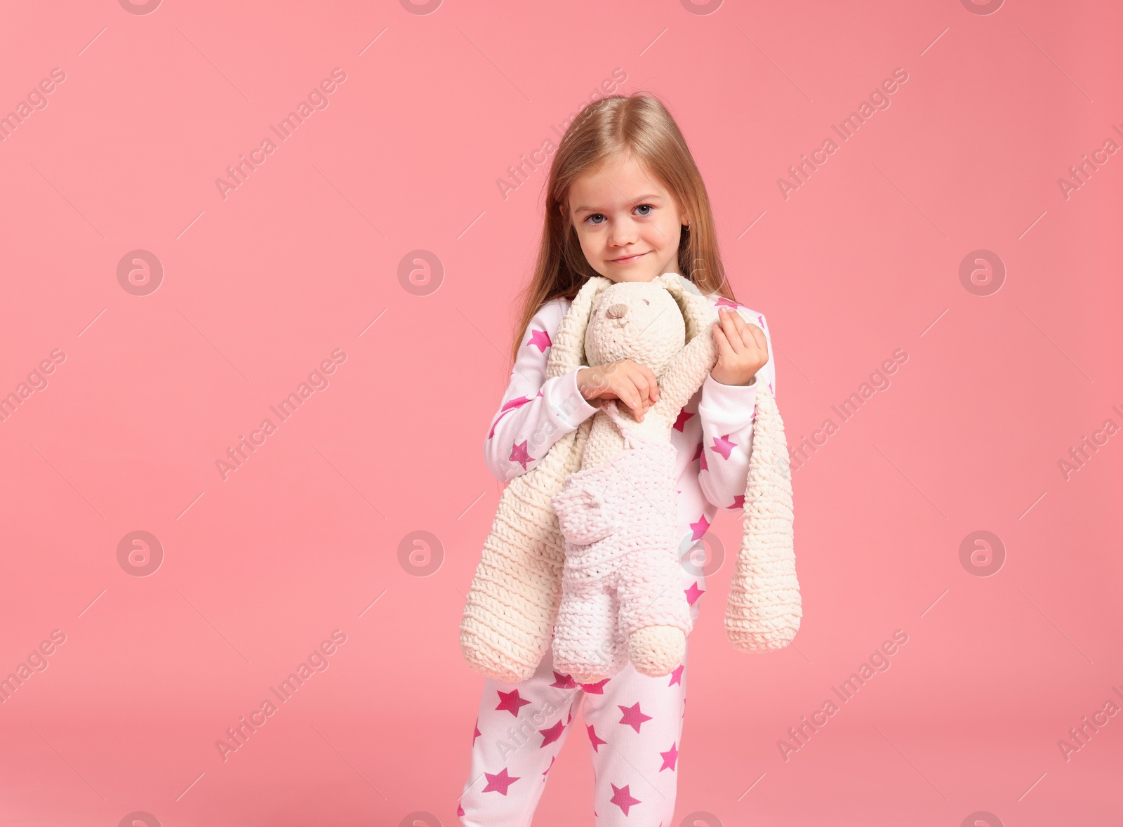Cute little girl in pajamas with toy bunny on pink background Photo of Cute little girl in pajamas with toy bunny on pink background