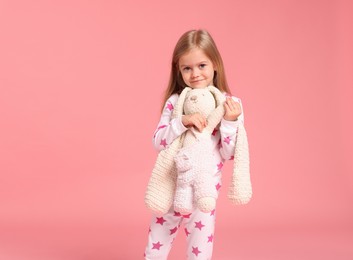 Photo of Cute little girl in pajamas with toy bunny on pink background